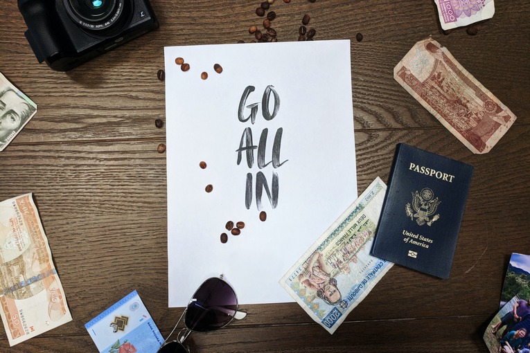 Picture of passports with currency and camera with paper that reads “go all in”