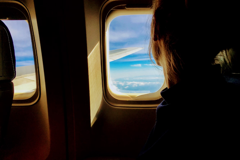 person looking out airplane window at sky and plane wing