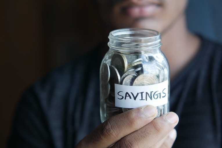 person holding jar labeled “savings” filled with coins