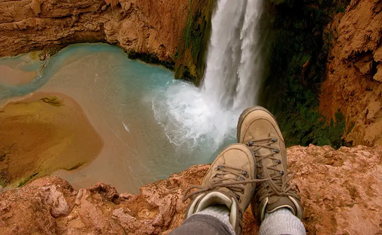 hiking boots on a cliffside looking out on a waterfall and pool below