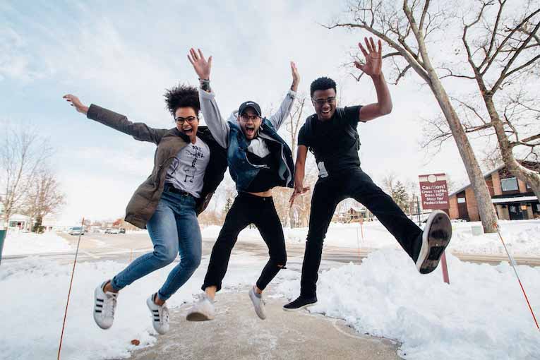 three people jumping on snowy sidewalk