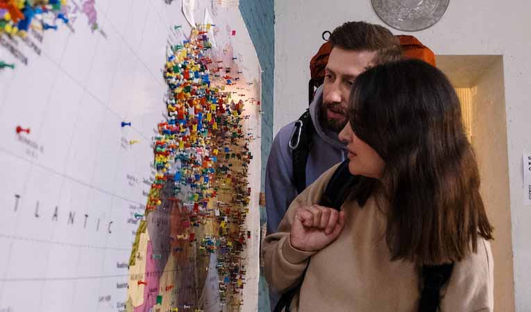 two backpackers observing a map full of pins on a hostel wall