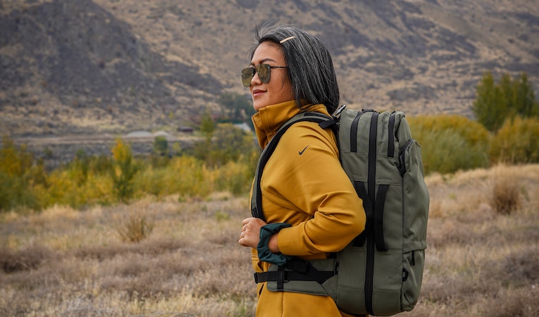 person in a yellow hoodie and sunglasses hiking with a backpack