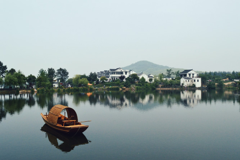 wooden boat on water with buildings, mountain, and trees behind