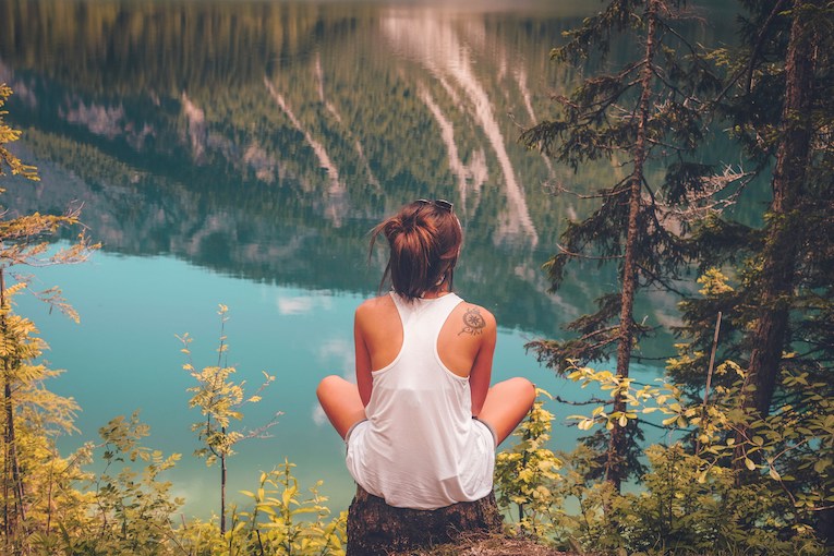 solo traveler sitting on a tree stump overlooking a blue lake in italy