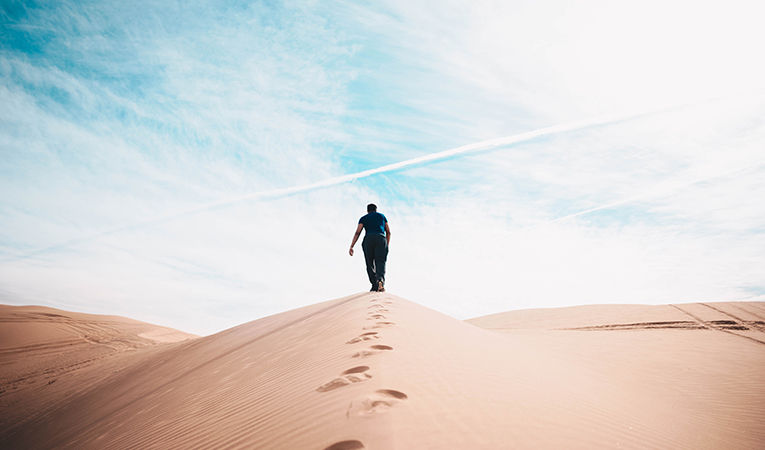 man hiking up a sand dune
