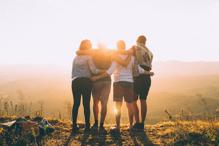 backs of four people with arms around each other watching sun set