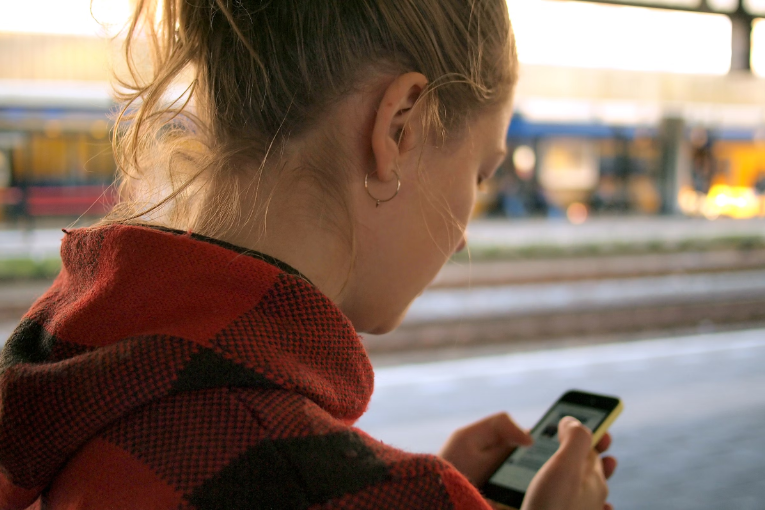 person at train station looking down at cell phone