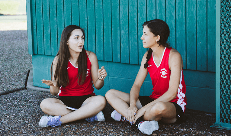 two teen girls in athletic gear sitting in shade